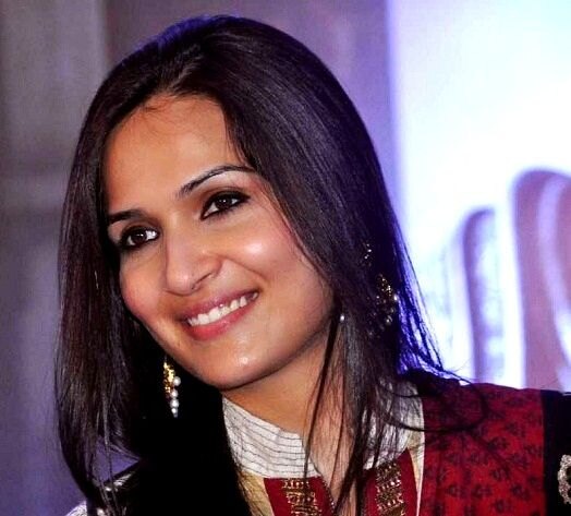 Close portrait of Soundarya Rajinikanth smiling, wearing a deep red outfit and gold jhumka earrings