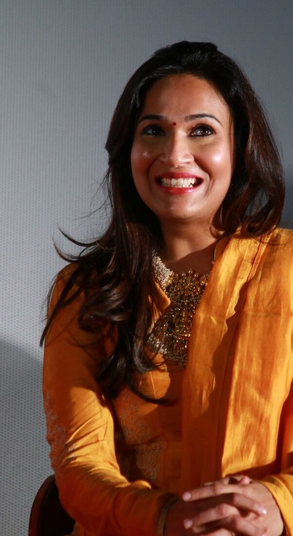 Soundarya Rajinikanth smiling in a marigold-yellow kurta at a press event