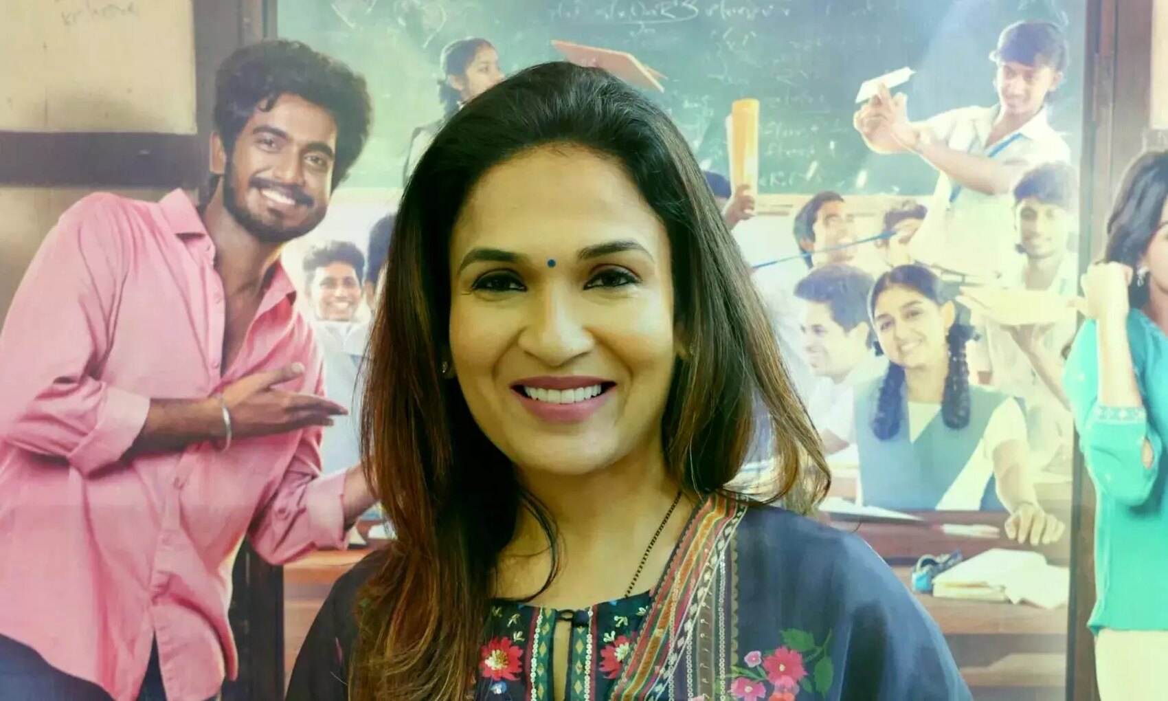 Soundarya Rajinikanth smiling at a recent film event, photographed in front of a printed film backdrop