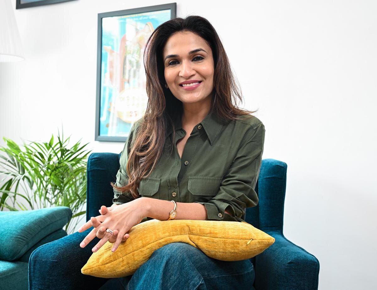 Soundarya Rajinikanth seated in a teal armchair wearing an olive shirt, photographed during an interview