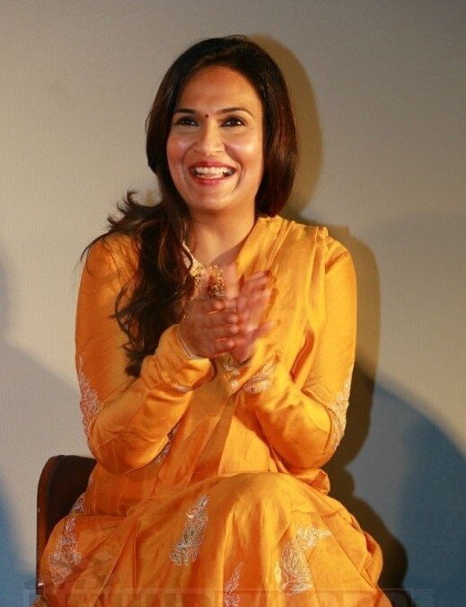 Soundarya Rajinikanth applauding, seated, in a marigold-yellow embroidered outfit at a film event