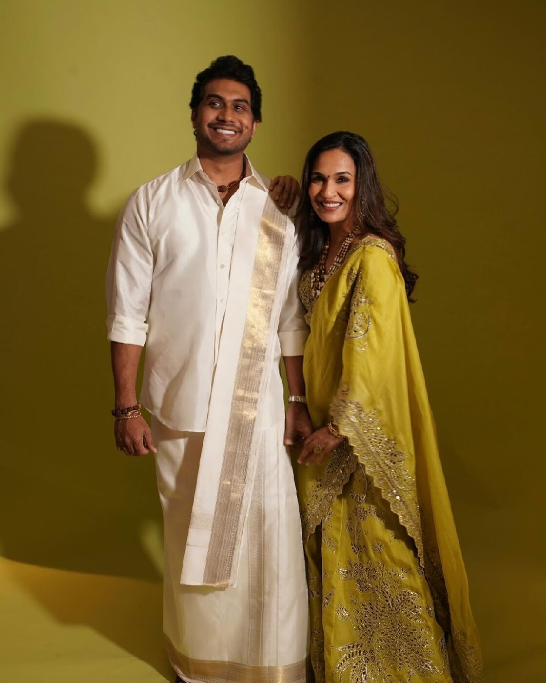 Soundarya Rajinikanth in a lime-green embroidered saree beside her husband Vishagan Vanangamudi in a white veshti, photographed in a studio against an olive backdrop