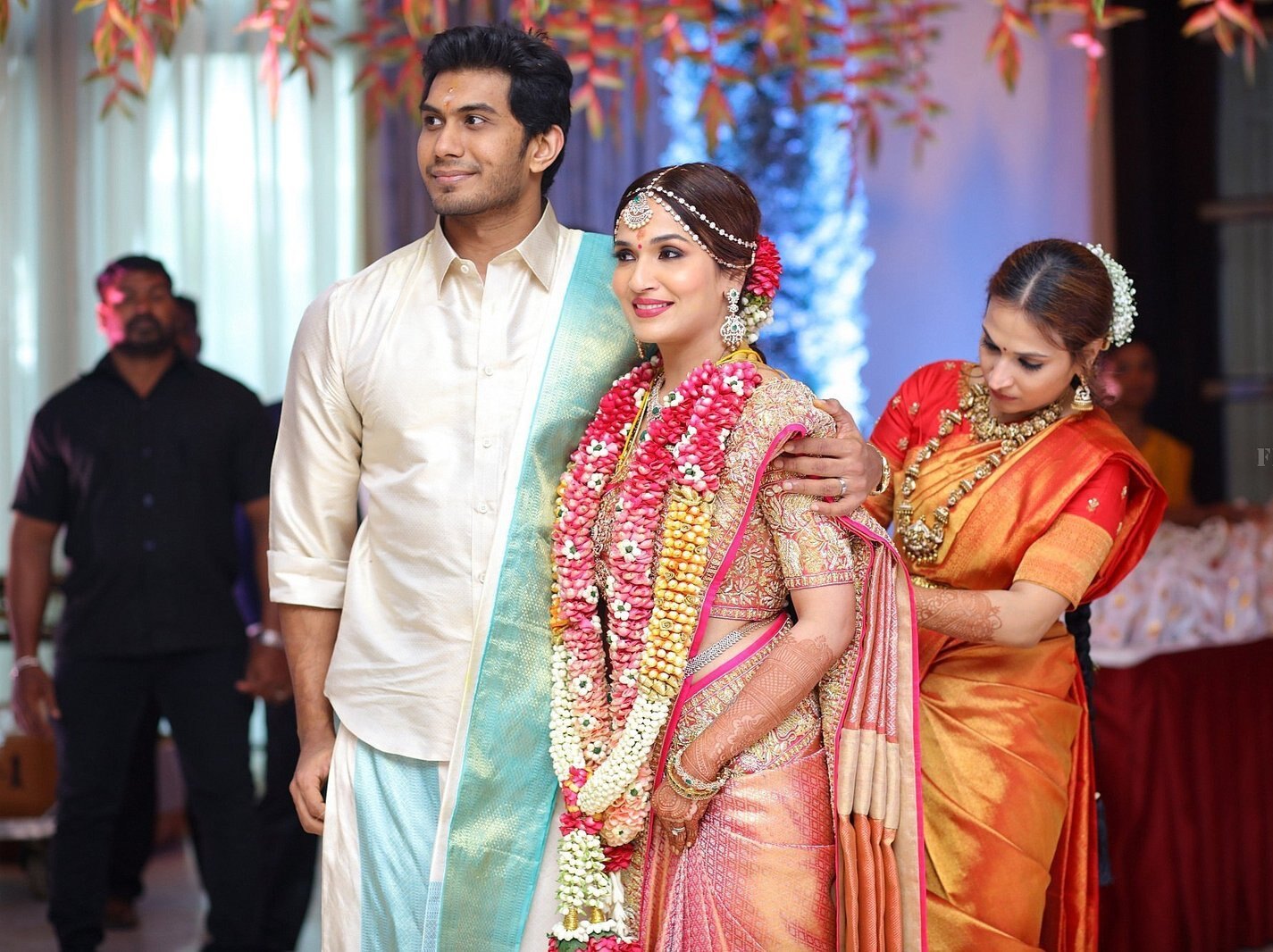 Soundarya Rajinikanth in bridal silk and floral garlands beside Vishagan Vanangamudi at their wedding ceremony, with her sister Aishwarya Rajinikanth adjusting her saree
