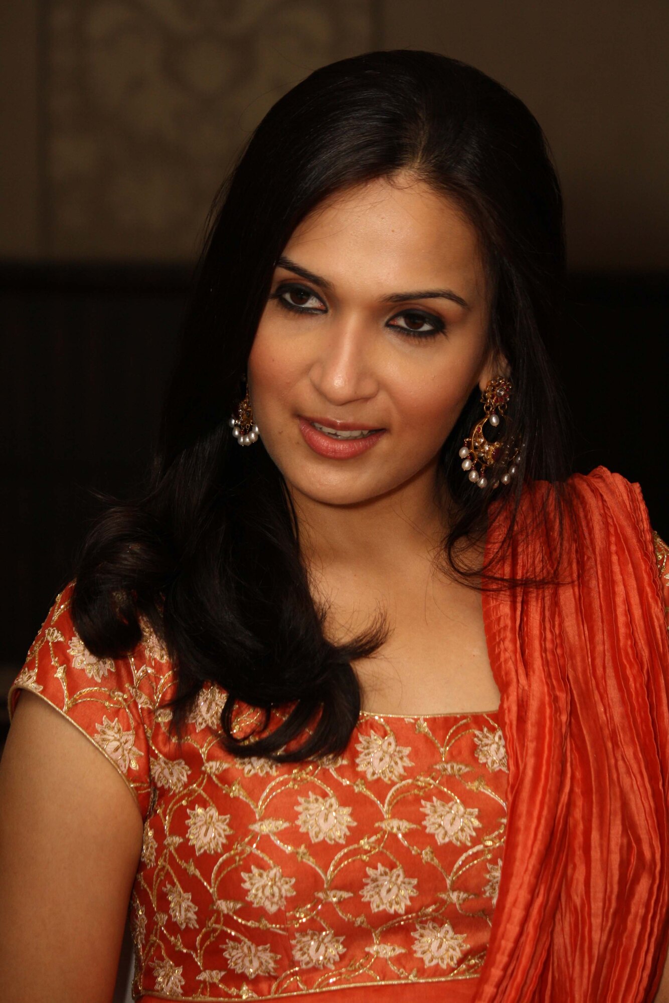 Portrait of Soundarya Rajinikanth in an embroidered orange anarkali, photographed against a dark background